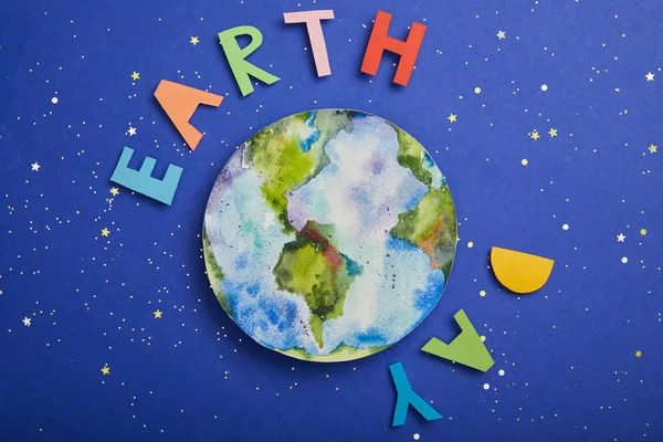 Draufsicht auf bunte Papierbuchstaben und Planetenbild auf violettem Hintergrund mit Sternen, Earth Day Konzept — Stockfoto