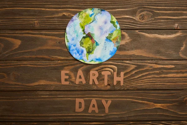 Draufsicht auf Papierbuchstaben und Planetenbild auf braunem Holzgrund, Earth Day Konzept — Stockfoto