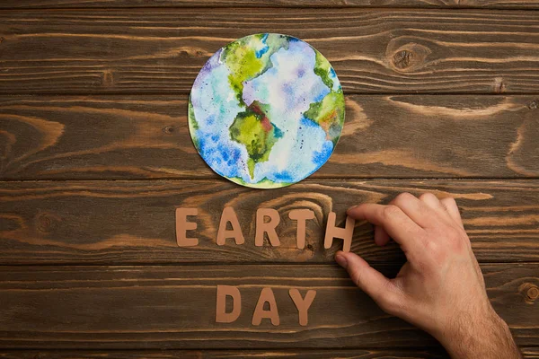 Teilansicht einer Frau mit Papierbuchstaben und Planetenbild auf braunem Holzgrund, Earth Day Konzept — Stockfoto