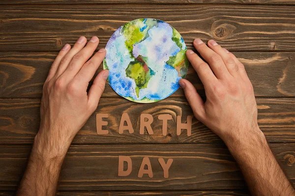 Teilansicht einer Frau mit Planetenbild und Papierbuchstaben auf braunem Holzgrund, Earth Day Konzept — Stockfoto
