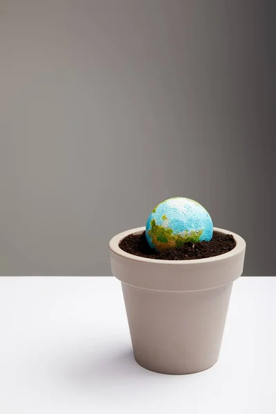 Modèle de planète placé dans un pot de fleurs avec du sol sur la surface de la table, concept de jour de la terre — Photo de stock