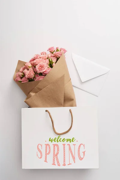 Bouquet of beautiful pink roses and white envelope near paper bag with welcome spring illustration — Stock Photo