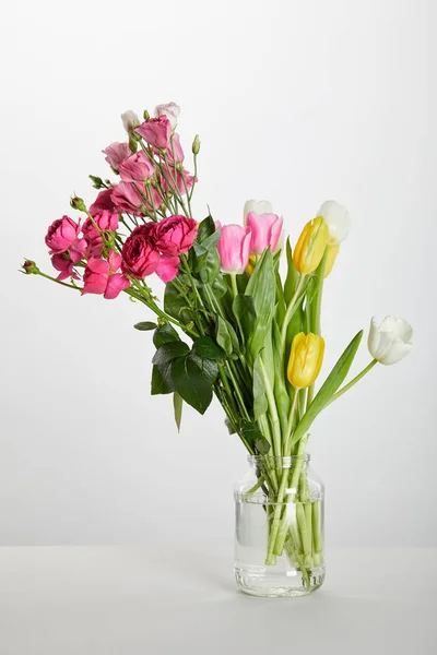 Rosas rosadas frescas y tulipanes amarillos en frasco de vidrio aislado en blanco - foto de stock