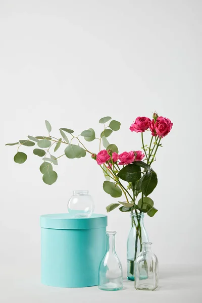 Roses roses fraîches et eucalyptus en bouteille transparente avec boîte cadeau turquoise isolé sur blanc — Photo de stock