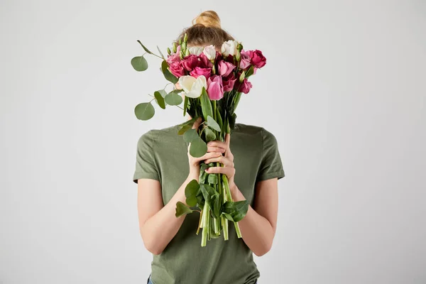 Girl holding bouquet with tulips, eucalyptus and roses in front of face isolated on grey with copy space — Stock Photo