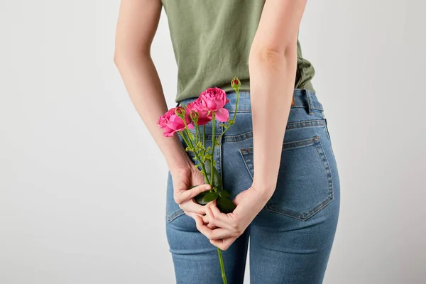 Vista trasera de la niña sosteniendo rosas rosadas aisladas en gris con espacio de copia - foto de stock