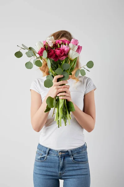 Fille tenant bouquet frais avec tulipes, eucalyptus et roses devant le visage isolé sur gris — Photo de stock