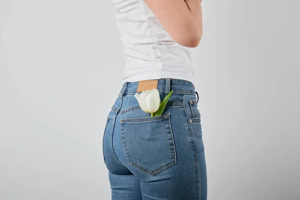 Cropped view of girl with tulip flower in jeans pocket isolated on grey — Stock Photo