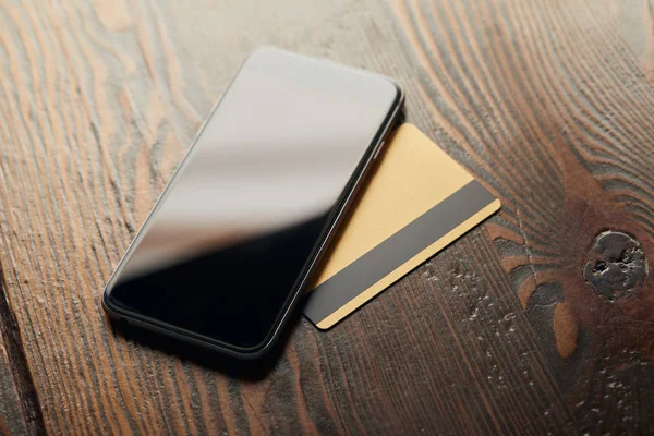 Tarjetas de crédito y smartphone con pantalla en blanco sobre mesa de madera - foto de stock