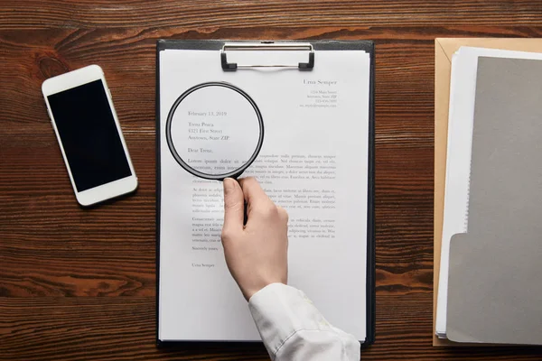 Cropped view of businessman reading contract on clipboard with loupe — Stock Photo