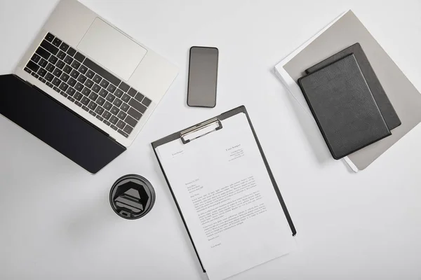 Top view of documet on clipboard, paper cup, laptop, smartphone, notebooks and folder — Stock Photo