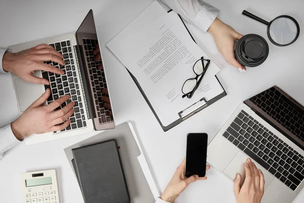 Vista superior de los empresarios escribiendo en computadoras portátiles, sosteniendo teléfono inteligente y taza de papel - foto de stock