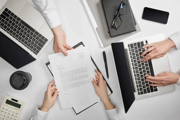 Top view of businesspeople typing on laptop and holding document — Stock Photo