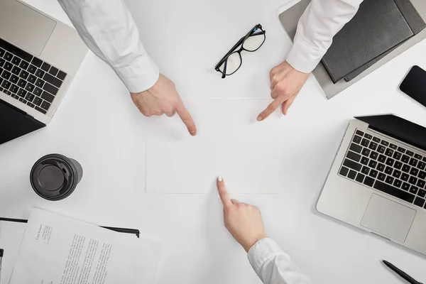 Top view of businesspeople pointing to blank paper at workplace — Stock Photo