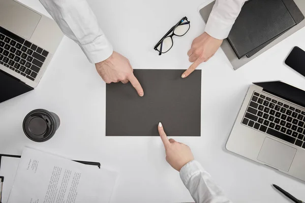 Top view of businesspeople pointing to blank grey paper at workplace — Stock Photo