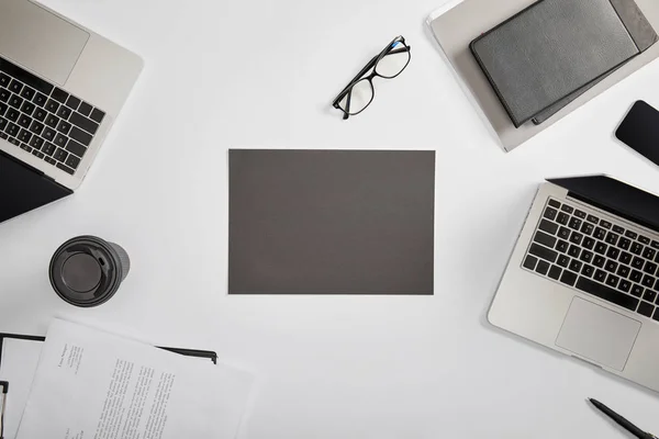 Top view of documet on clipboard, paper cup, laptops, pen, notebooks, folder, glasses and grey paper — Stock Photo