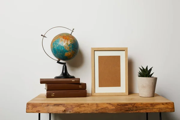 Globe sur les livres près du cadre et plante en pot sur la table — Photo de stock