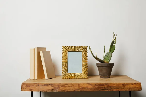 Libros cerca de marco dorado y cactus en maceta sobre mesa de madera — Stock Photo