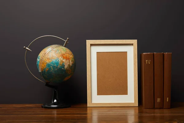 Globe near blank frame and books on table — Stock Photo