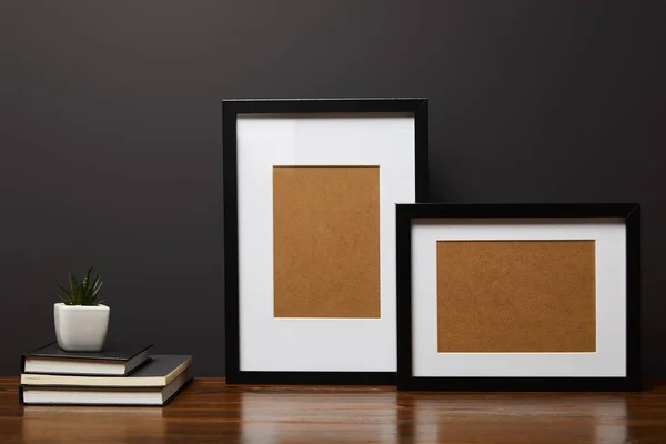 Black square frames near books and plant on wooden table — Stock Photo