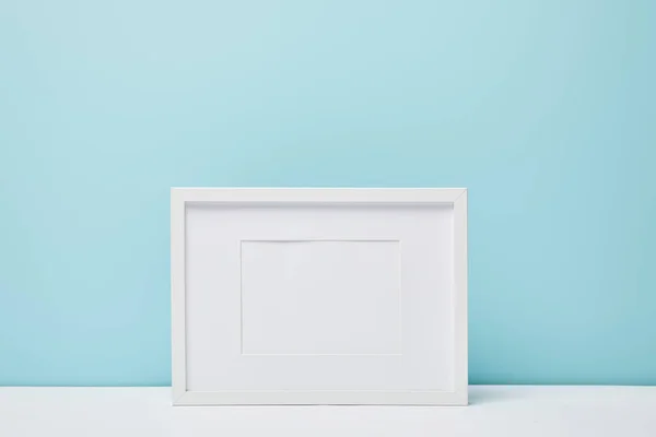 Quadro quadrado branco na superfície branca perto da parede azul — Fotografia de Stock