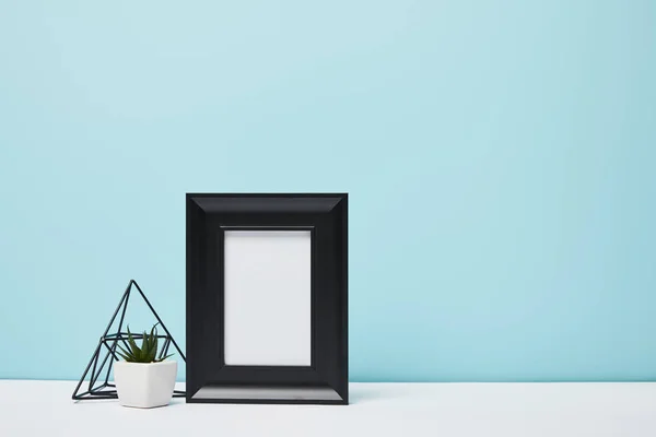 Black square frame near green plant on white surface — Stock Photo