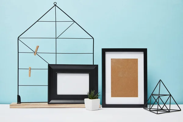 Black frames near green plant in pot and metallic holders on table — Stock Photo