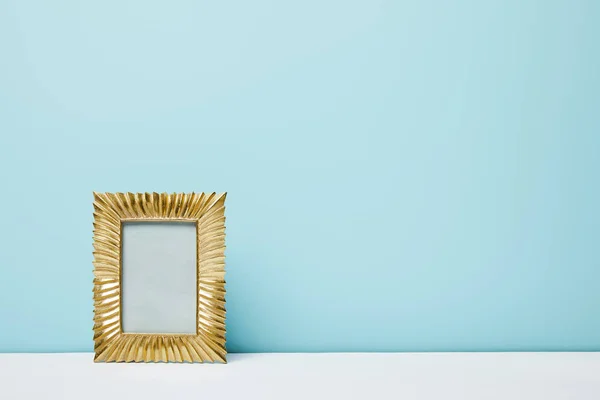 Золотая рамка на белой поверхности возле голубой стены — стоковое фото