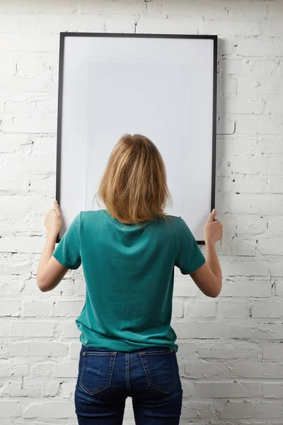 Visão traseira da mulher segurando mock up cartaz com moldura preta — Fotografia de Stock