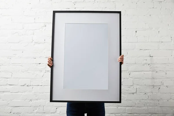 Mujer cubriendo la cara mientras sostiene el marco negro en blanco - foto de stock