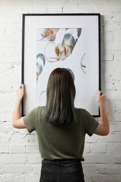 Back view of woman holding drawing in black square frame in hands — Stock Photo