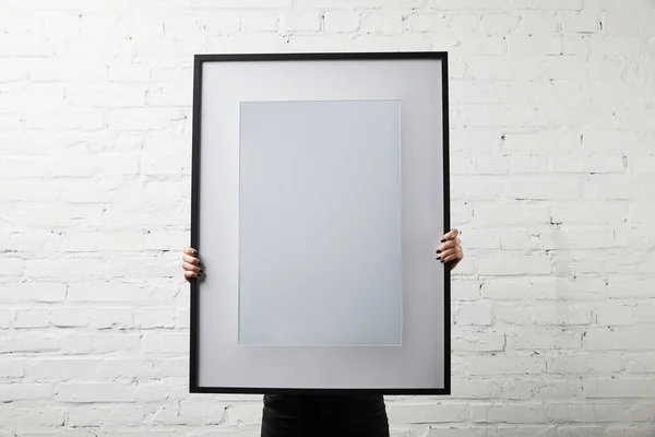 Woman covering face while standing and holding blank black frame — Stock Photo