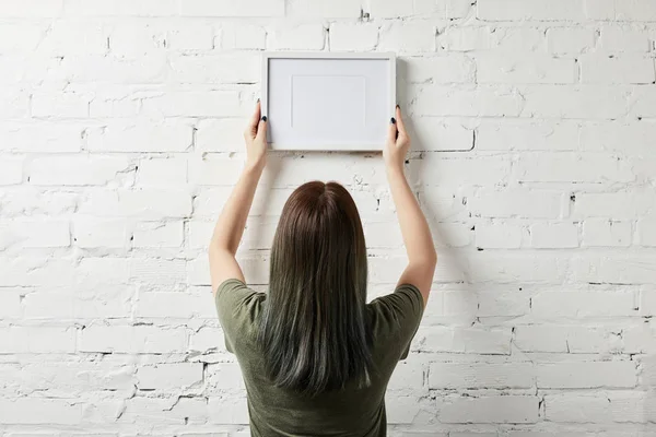 Back view of woman holding blank white square frame in hands — Stock Photo