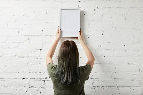 Vista posterior de la mujer sosteniendo el marco blanco en blanco en las manos - foto de stock