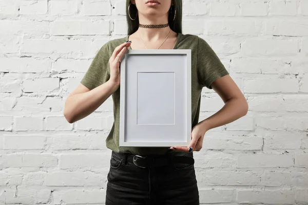 Vista ritagliata della donna in piedi e tenendo vuota cornice bianca in mano — Foto stock