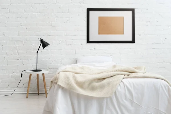 Современная спальня с кроватью и черной рамкой на белой кирпичной стене — стоковое фото