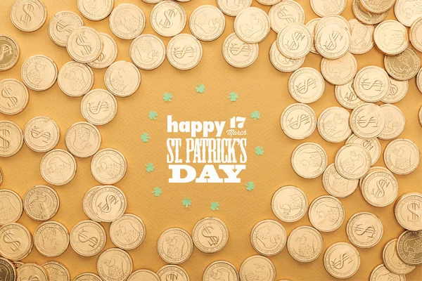 Vista superior de las monedas de oro con signos de dólar y círculo de tréboles cerca de feliz día st patricks letras sobre fondo naranja - foto de stock