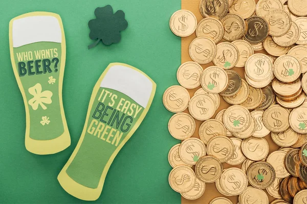 Top view of golden coins with dollar signs, shamrock and paper beer glasses with lettering on green background — Stock Photo