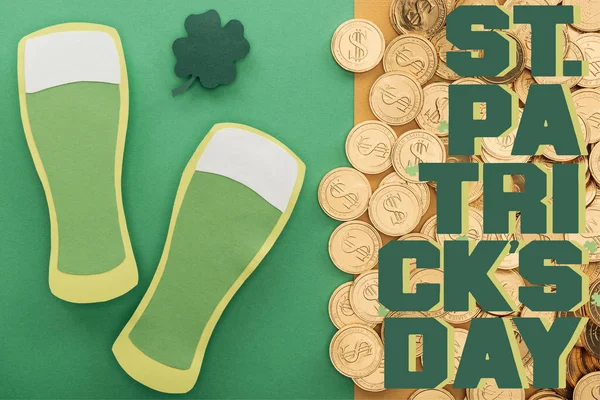 Top view of golden coins with dollar signs, shamrock and paper beer glasses with st patrick day lettering on green background — Stock Photo