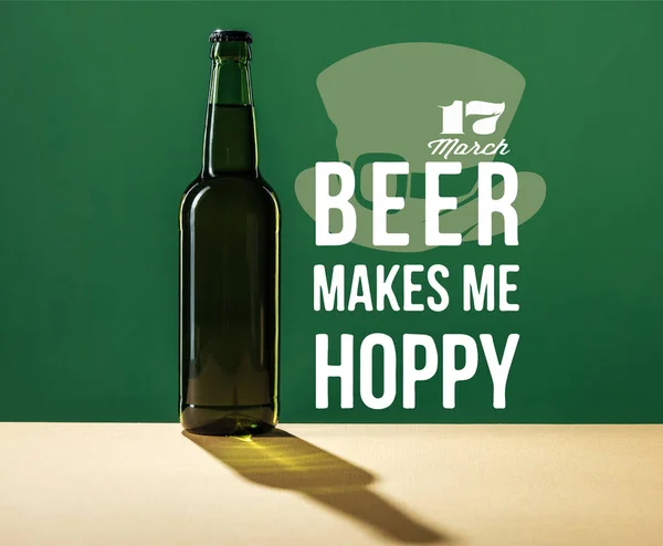 Glass beer bottle near beer makes me hoppy lettering on green background — Stock Photo