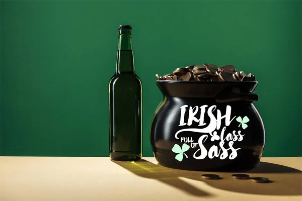 Пляшка пива і чорний горщик з золотими монетами з ірландським лайном, повним лосьйонів на зеленому фоні — стокове фото