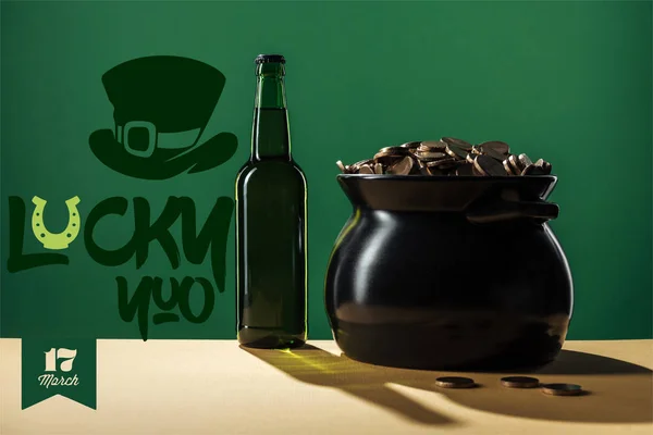 Botella de cerveza y olla negra con monedas de oro cerca de suerte que las letras sobre fondo verde - foto de stock
