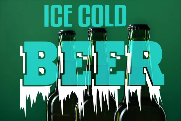 Beer bottles near ice cold beer lettering on green background — Stock Photo