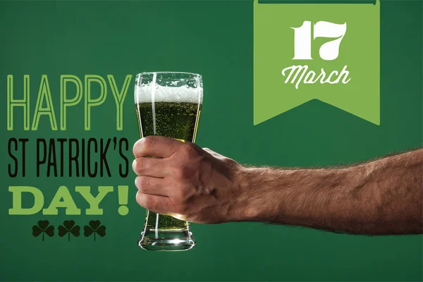 Cropped view of man holding glass of beer with foam near happy st patricks day lettering on green background — Stock Photo