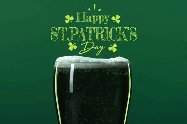 Glass of beer with foam near happy st patricks day lettering on green background — Stock Photo