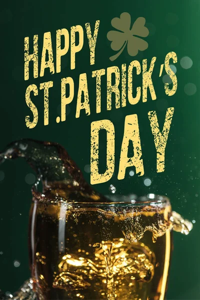 Glass of beer with splash near happy st patricks day lettering on green background — Stock Photo