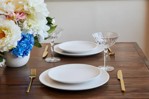 Teller, goldene Messer und Gabeln mit Kristallgläsern und Blumen in Vase auf Holztisch im Restaurant — Stockfoto