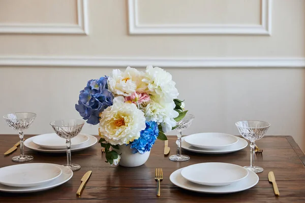 Piatti, coltelli e forchette, bicchieri di cristallo e bouquet in vaso bianco su tavolo di legno nel ristorante — Foto stock