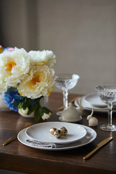 Selective focus of quail eggs on white plates, flowers and crystal glasses on wooden table at home — Stock Photo