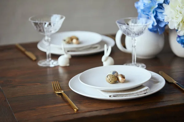 Selective focus of quail eggs on white plates, crystal glasses and decorative bunnies on wooden table at home — Stock Photo